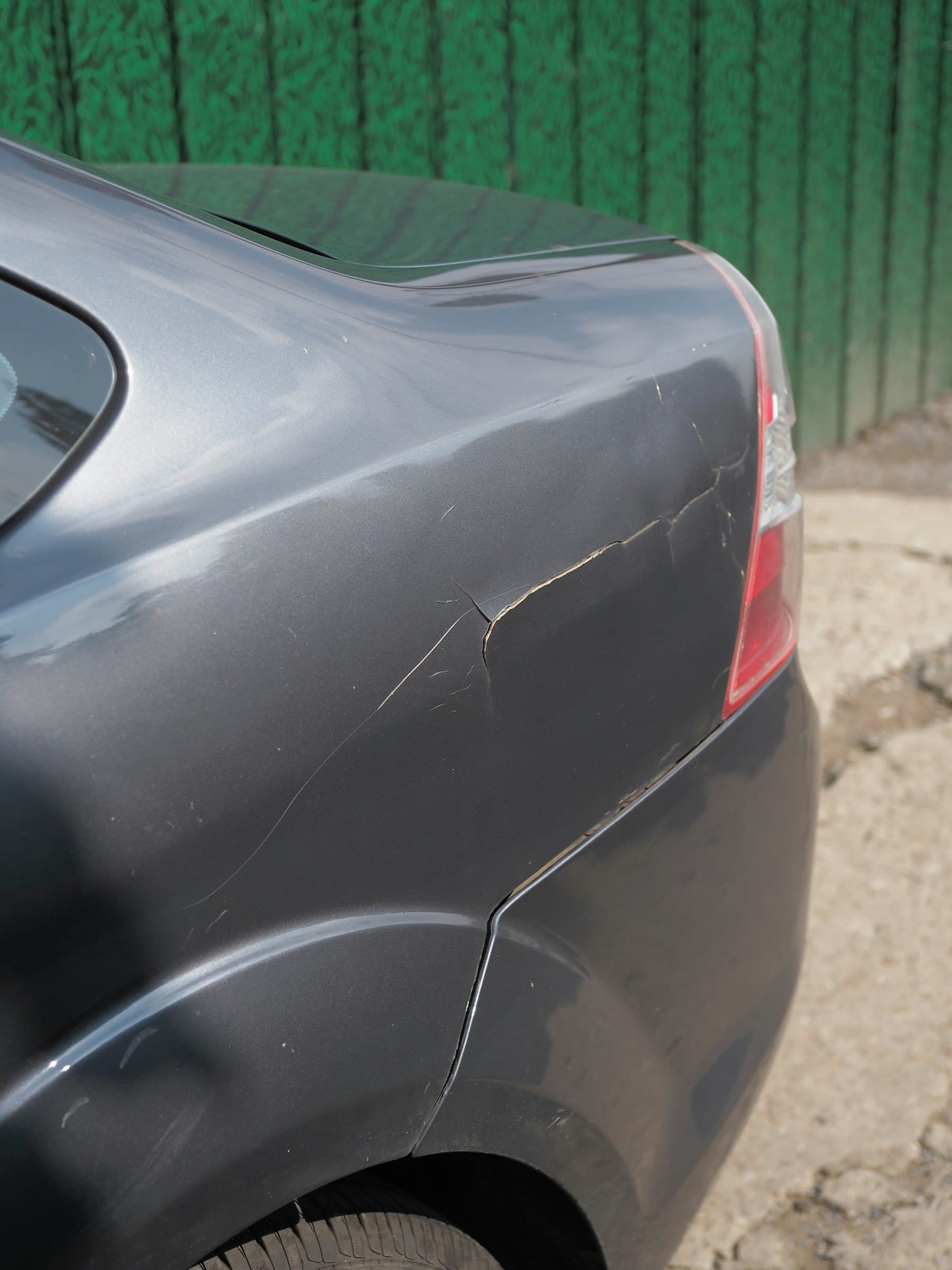 Close-up of a dented grey car panel with cracked paint