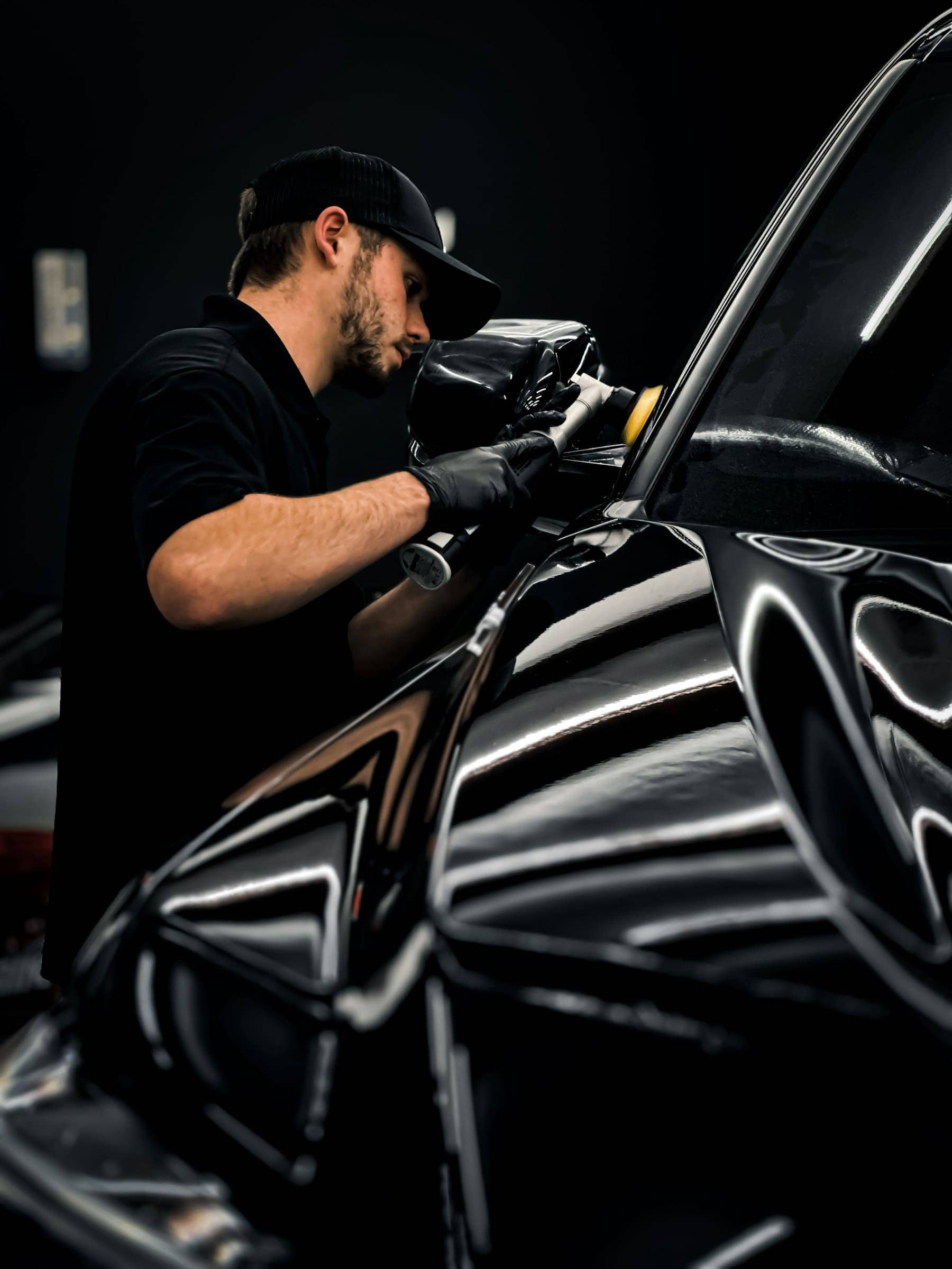 Technician machine-polishing the glossy black paintwork of a car